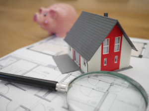 magnifying glass over blueprint with house and piggy bank