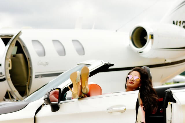 woman in white convertible with plane in back
